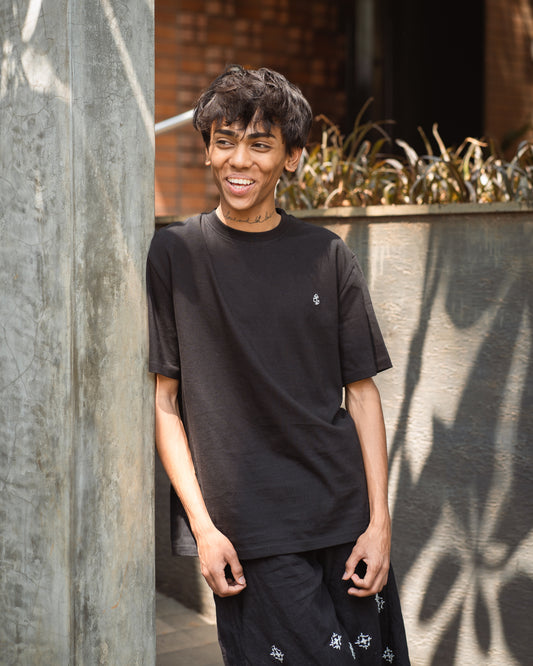 Man smiling and leaning casually against a wall in black organic cotton T-shirts from 2512 Pacchis Barah — showcasing the relaxed vibe of sustainable t-shirts and eco friendly t-shirts made for everyday wear. This lightweight organic cotton tee fits both men’s organic cotton t shirts and organic t shirts women ranges.