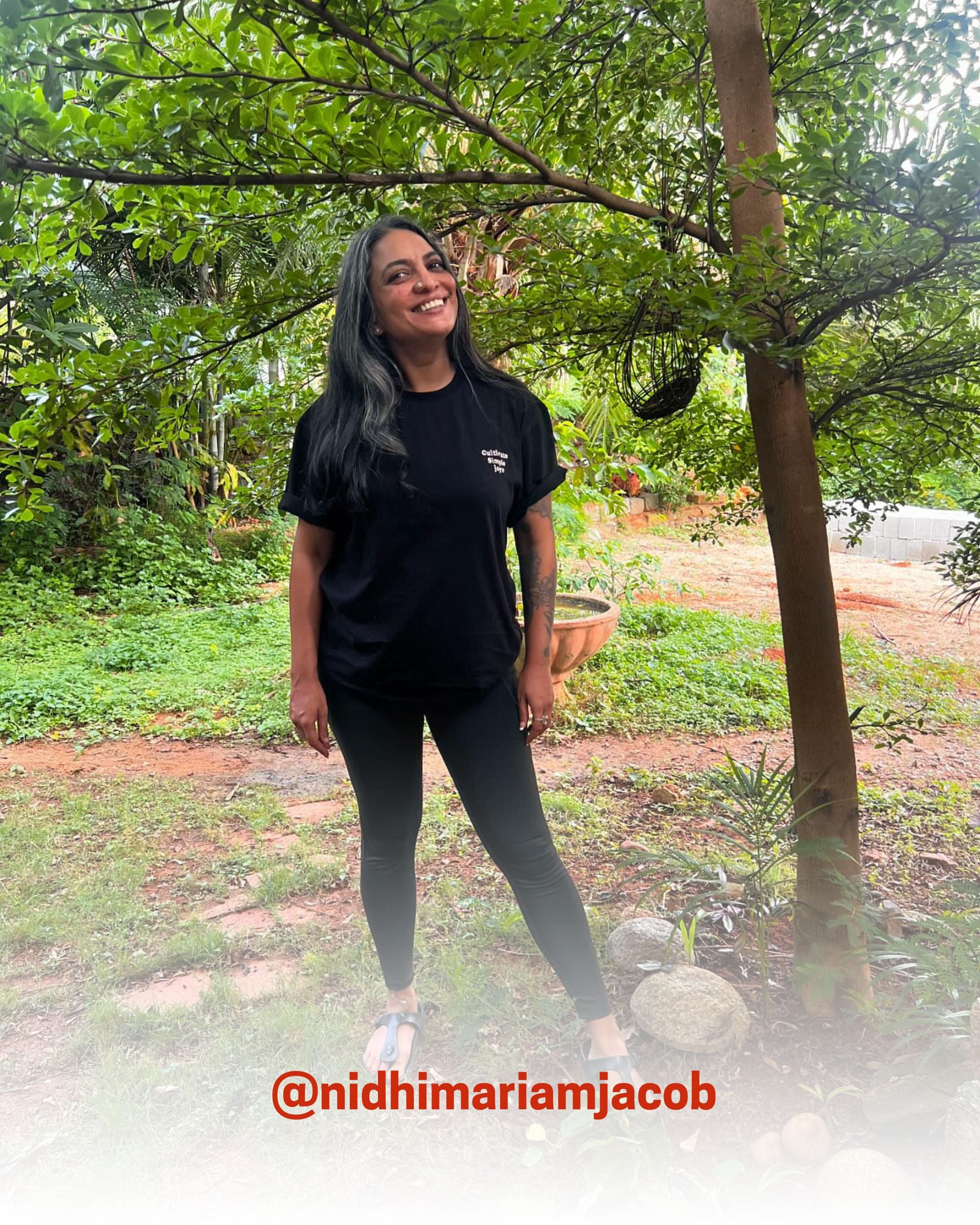 Smiling woman wearing a black organic cotton T-Shirt in a garden, showcasing 2512’s sustainable t-shirts, a creator favorite eco friendly tee.