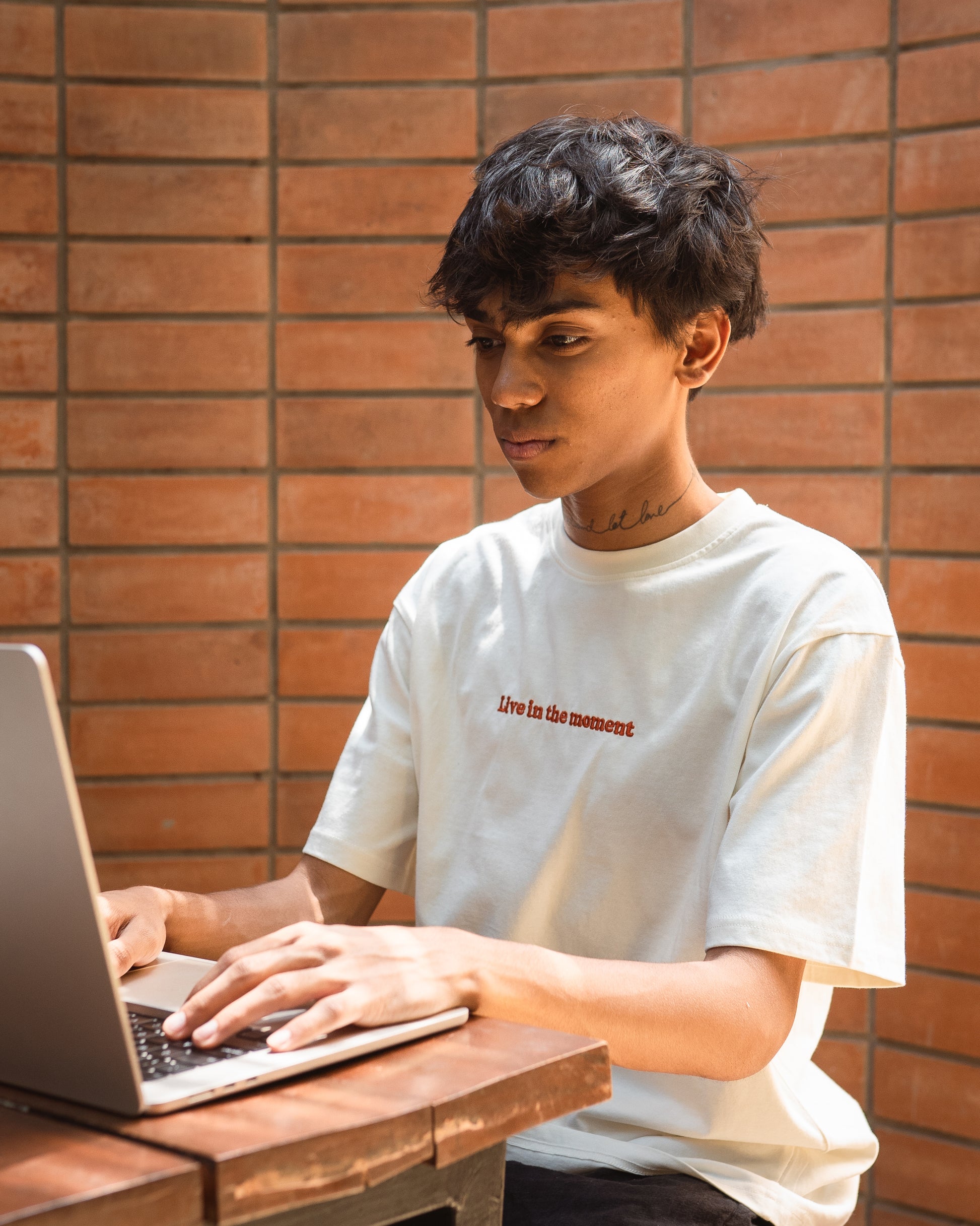 Model wearing white organic cotton unisex t-shirt with 'Live in the Moment' embroidery, front view