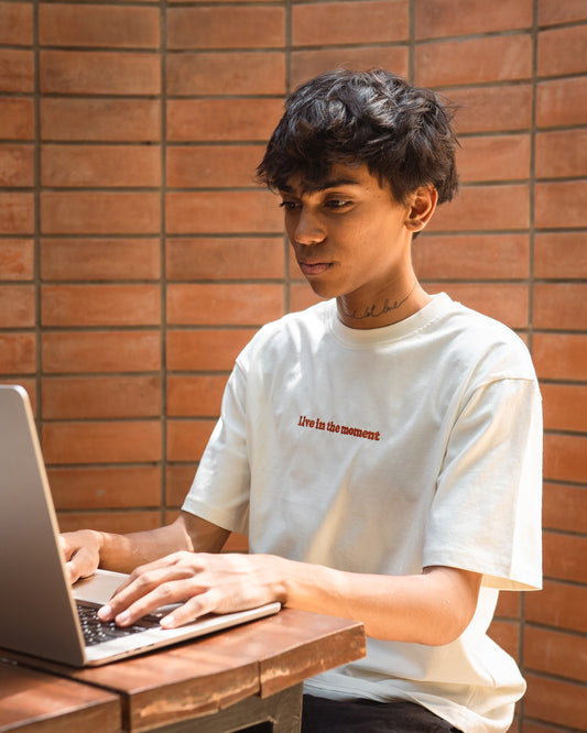 Model wearing white organic cotton unisex t-shirt with 'Live in the Moment' embroidery, front view